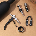 Arenzza wine opener set including corkscrew, foil cutter, and stopper, displayed on a wooden surface with wine bottles in the background.