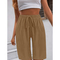 A woman wearing beige loose-fitting casual solid-color shorts by Arenzza, styled with a white top and belt.