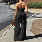 A woman wearing a strapless crinkle wide-leg jumpsuit by Arenzza, showcasing the relaxed fit and textured fabric.