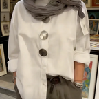 A woman wearing an oversized Arenzza women's button-down shirt with statement buttons, styled casually in a bright, modern setting.