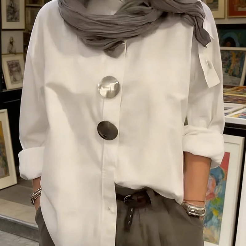 A woman wearing an oversized Arenzza women's button-down shirt with statement buttons, styled casually in a bright, modern setting.