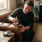 A person applying Arenzza leather balm to restore shine and prevent cracks on a leather bag in a lifestyle setting.