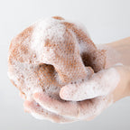 Arenzza African exfoliating net in natural fiber for skin scrubbing and exfoliation, shown hanging in a bathroom setting.